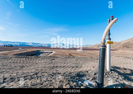 Eine vertikale Deponie Methangasbrunnen an einer aktiven Deponie, die die riesige abgeflachte Ausdehnung im Hintergrund zeigt. Stockfoto