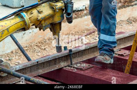 Bahnarbeiter, die die Gleisschiene verschrauben. Detailarbeiter mit mechanischem Schraubenschlüssel Stockfoto