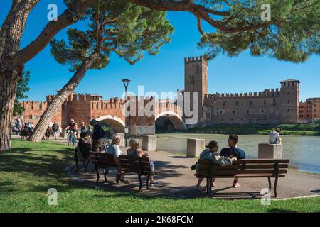 Verona Italien Brücke, Blick im Sommer von Menschen entspannen auf Bänken in der Nähe der malerischen Ponte Scaligero in der historischen Stadt Verona, Italien Stockfoto