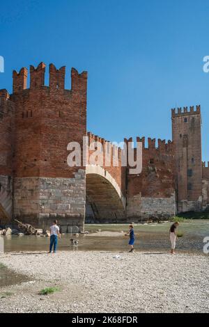 Brücke Verona, Blick im Sommer auf die Ponte Scaligero und junge Menschen, die entlang der Etsch in der historischen Stadt Verona, Italien stehen Stockfoto