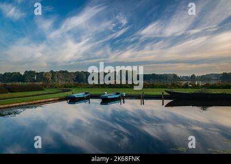 Ruderboote werden im Erholungsgebiet 't Weegje in der Nähe von Gouda, Niederlande, vertäut. Schöne Spiegelungen von Wolken im ruhigen Wasser. Stockfoto