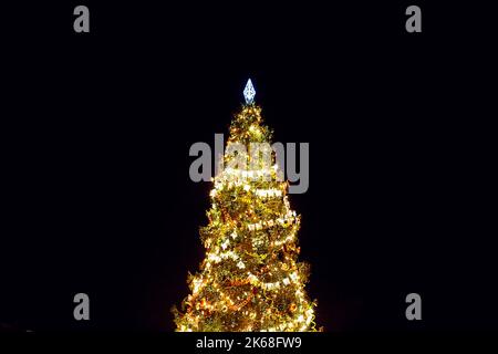 Vintage Weihnachtsbaum mit reichen Dekorationen.Weihnachtsornament hängt auf Baum Zweig. Glänzende Girlande goldene Lichter. Retro-Spielzeug und Licht Girlande Stockfoto