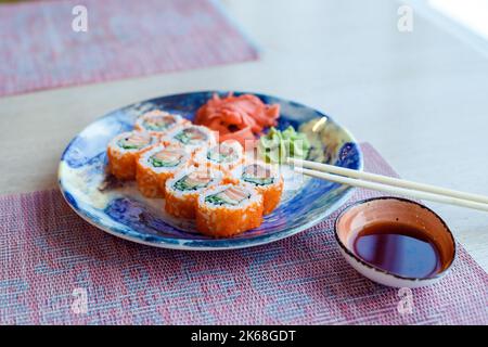 Sushi-Rolle, Philadelphia, mit Lachs, geräuchertem Aal, Avocado, Frischkäse auf blauem Teller. Sushi-Menü. california Roll. Sushi mit Essstäbchen. japanisch Stockfoto