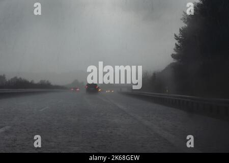 Starker Regen auf der Autobahn, verschwommene Autos mit roten Schlussleuchten, Tropfen und Wasser auf der dunklen Straße, gefährliches Wetter während der Fahrt, Verkehr und Transport Stockfoto