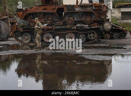 Lyman, Ukraine. 11. Oktober 2022. Ein ukrainischer Soldat steht neben einem zerstörten Panzer in Lyman, einer kürzlich von russischen Truppen befreiten Stadt in der Region Donezk. Mindestens 32 ukrainische Soldatenleichen wurden aus einem Massengrab in Lyman, einer Stadt im Donezker Gebiet, die unter russischer Besatzung stand, exhumiert. Die Behörden sagten, dass sie zusammen begraben wurden und erste Untersuchungen zeigten, dass einige Leichen mit verbundenen Augen und an den Händen gebunden waren, was Anzeichen von Folter und Hinrichtung nahelegt. Weitere 22 Zivilisten, darunter auch Kinder, wurden von einer anderen Begräbnisstätte in der Nähe exhumiert. Beide Standorte liegen Stockfoto