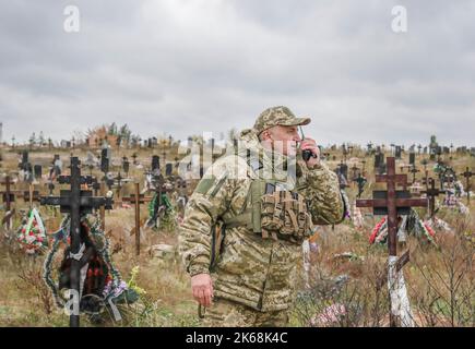 Lyman, Ukraine. 11. Oktober 2022. Auf einem Friedhof in Lyman steht ein ukrainischer Soldat. Nach der Befreiung der Stadt von russischen Truppen im Donezker Gebiet wurde neben dem Friedhof von den Ukrainern eine Grabstätte entdeckt. Mindestens 32 ukrainische Soldatenleichen wurden aus einem Massengrab in Lyman, einer Stadt im Donezker Gebiet, die unter russischer Besatzung stand, exhumiert. Die Behörden sagten, dass sie zusammen begraben wurden und erste Untersuchungen zeigten, dass einige Leichen mit verbundenen Augen und an den Händen gebunden waren, was Anzeichen von Folter und Hinrichtung nahelegt. Weitere 22 Zivilisten, darunter Kinder wir Stockfoto