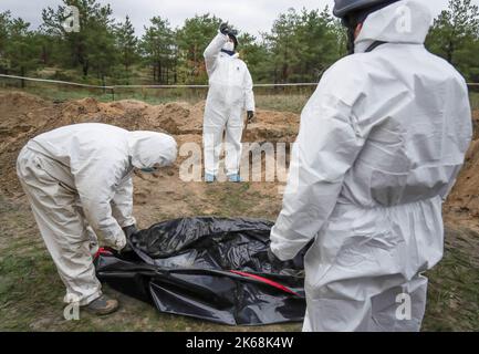 Lyman, Ukraine. 11. Oktober 2022. Ermittler werden gesehen, wie sie in Lyman einen Leichensack mit exhumiertem Körper zippen. Mindestens 32 ukrainische Soldatenleichen wurden aus einem Massengrab in Lyman, einer Stadt im Donezker Gebiet, die unter russischer Besatzung stand, exhumiert. Die Behörden sagten, dass sie zusammen begraben wurden und erste Untersuchungen zeigten, dass einige Leichen mit verbundenen Augen und an den Händen gebunden waren, was Anzeichen von Folter und Hinrichtung nahelegt. Weitere 22 Zivilisten, darunter auch Kinder, wurden von einer anderen Begräbnisstätte in der Nähe exhumiert. Beide Standorte befinden sich am Rande eines Friedhofs. Beamte sagten, dass sie erwartet würden Stockfoto