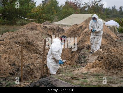 Lyman, Ukraine. 11. Oktober 2022. Ermittler, die Schutzkleidung tragen, werden gesehen, wie sie die Leichen ukrainischer Soldaten von einer Begräbnisstätte in Lyman exhumieren. Mindestens 32 ukrainische Soldatenleichen wurden aus einem Massengrab in Lyman, einer Stadt im Donezker Gebiet, die unter russischer Besatzung stand, exhumiert. Die Behörden sagten, dass sie zusammen begraben wurden und erste Untersuchungen zeigten, dass einige Leichen mit verbundenen Augen und an den Händen gebunden waren, was Anzeichen von Folter und Hinrichtung nahelegt. Weitere 22 Zivilisten, darunter auch Kinder, wurden von einer anderen Begräbnisstätte in der Nähe exhumiert. Beide Standorte liegen am Rande eines ceme Stockfoto