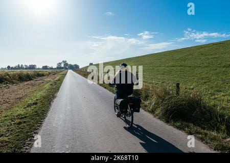 Frau auf dem Fahrrad hinter dem Deich auf dem Weserradweg südlich von Bremerhaven. Stockfoto