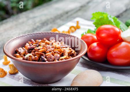 Gebratene Waldpilze Pfifferlinge mit Zwiebel in rustikaler Schüssel und Teller mit frischem Gemüse für Salat auf dem Hintergrund Stockfoto