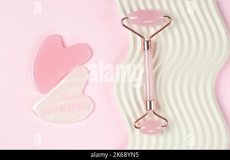 Gesichtsmassager mit Rolljade. Gua Sha Gesichtsmassagewerkzeuge auf rosa Hintergrund Stockfoto
