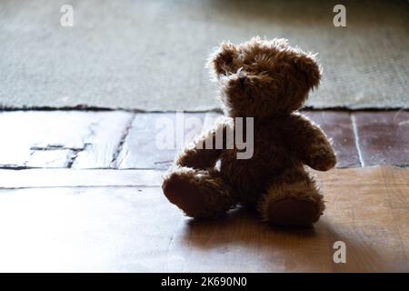 Brauner Teddybär sitzt auf einem alten Holzboden in einem dunklen Raum, Kinderspielzeug auf dem Boden, Angst Stockfoto