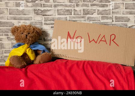 Stop war je geschrieben auf Schild die steht zu Hause in der Ukraine in der Nähe eines Teddybären mit Flagge der Ukraine. Frieden in der Ukraine. Protest. Russland ist der Aggressor 2022 Stockfoto