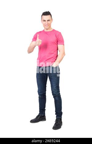 Selbstbewusster junger Mann, der den Daumen nach oben deuchte und die Kamera anlächelte Stockfoto