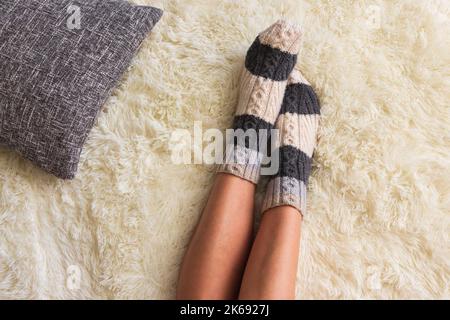 Mädchen in warmen Wollsocken mit Kissen, Draufsicht. Frau auf weißer Decke. Gemütliche Innenausstattung. Konzept für Winterferien. Komfortable Entspannung. Komfort zu Hause. Stockfoto