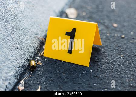 Ein gelber Tatort-Marker auf der Straße, nach einer Schießerei mit einer Messingkugelschale, die eine 9mm-Pistole umhüllt Stockfoto