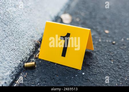 Ein gelber Tatort-Marker auf der Straße, nach einer Schießerei mit einer Messingkugelschale, die eine 9mm-Pistole umhüllt Stockfoto