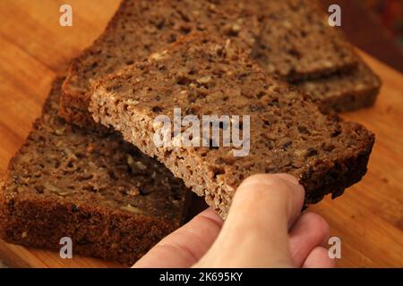 Die Hand der Frau nimmt Vollkornbrot, Nahaufnahme. Unschärfe-Effekte. Gesundes Lebensmittelkonzept. Stockfoto