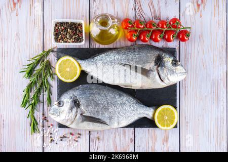 Dorado Fisch auf weißem Holzhintergrund. Meeresfrüchte mit Zutaten zum Kochen. Delikatesse Gewürze und Gemüse, Hintergrund für Menü und Restaurant reci Stockfoto