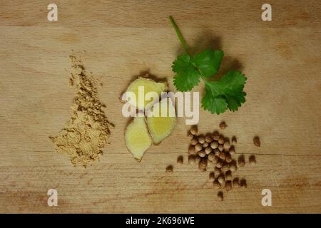 Ingwerwurzel und Pulver sowie Korianderfrüchte und Blätter auf Holzgräber. Nahaufnahme von oben. Stockfoto