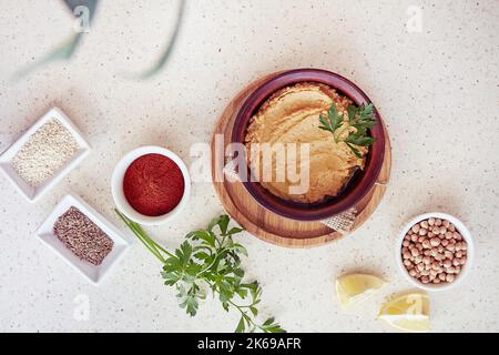 Hummus in der Schüssel, Petersilie, Zitrone, Paprika, römischer Kreuzkümmel, Kichererbsen, Sesamzutaten. Vegetarisch gesunde natürliche rustikale Lebensmittel Stockfoto