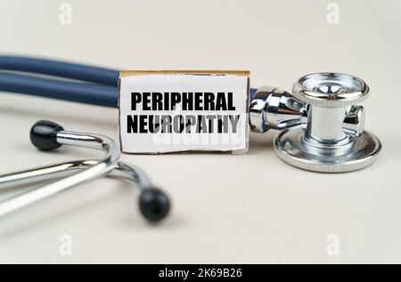 Medizinisches Konzept. Auf grauem Hintergrund ein Stethoskop und ein Pappschild mit der Aufschrift - peripherale Neuropathie Stockfoto