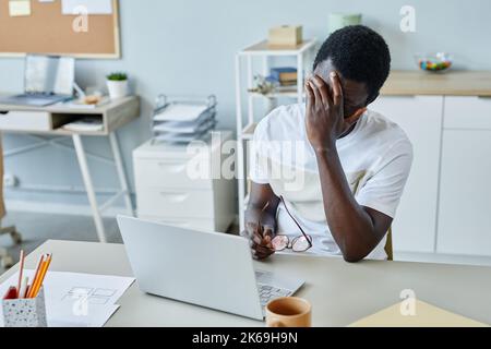 Porträt eines frustrierten schwarzen Mannes am Arbeitsplatz, der die Brille auszieht und unter Kopfschmerzen leidet Stockfoto