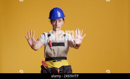 Portrait eines Bauarbeiters, der ein Stoppschild mit Handfläche macht, die Werbung geht nicht vorbei und beendet die Geste im Studio. Eine Fremdfirma, die nach den Arbeiten an der Sanierung das Symbol für das Ende der Zeitüberschreitung zeigt. Stockfoto