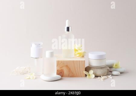 Kosmetische Hautpflegeprodukte mit Holzpodest und Blumen, Stein auf grauem Hintergrund. Nahaufnahme, Kopierbereich Stockfoto