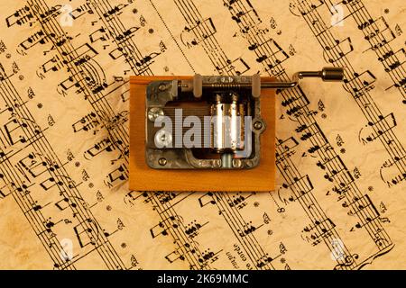 Spieluhr und Notizen. Souvenir-Musikbox auf dem Hintergrund alter Noten. Handorgan für klassische und moderne Melodie. Rückwirkender zylindrischer Mechanismus Stockfoto