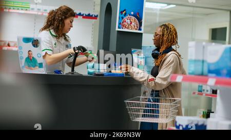 Apotheker, der medizinische Produkte an afroamerikanische Kunden verkauft und Medikamente und Nahrungsergänzungsmittel an der Apotheke kauft. Arbeiter scannen Kisten mit Medikamenten und Vitaminen, um Medikamente zu verkaufen. Handgeführte Aufnahme. Stockfoto