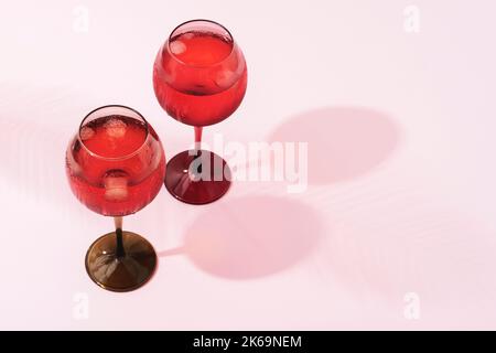 Kaltes Getränk mit Eis in Weinläsern, tropischer Palmenblatt-Schatten auf rosa Hintergrund. Stockfoto