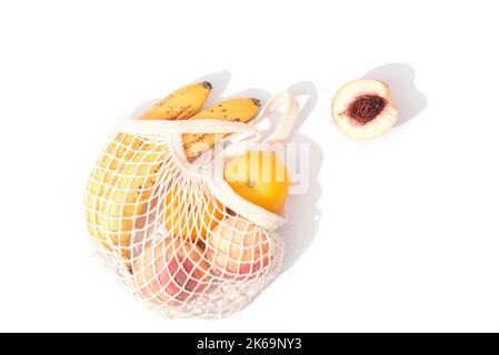 Bananen, Mandarinen und Pfirsiche im Saitenbeutel auf weißem Hintergrund mit Schatten. Vegane Rohkost. Zero Waste Konzept. Draufsicht, flach liegend. Stockfoto