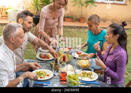 Frau serviert das Essen mit Freunden glücklich um den Tisch. Stockfoto