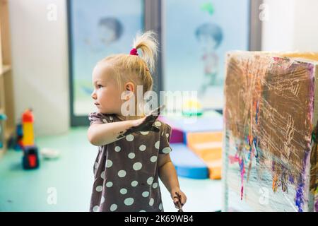 Blonde und kaukasische kleine Mädchen Malerei mit ihren Händen in der Kinderstube, mittlere Aufnahme verschwommener Hintergrund. Hochwertige Fotos Stockfoto