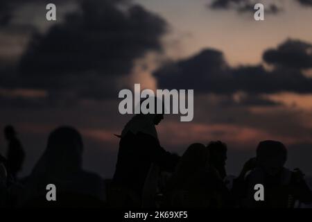 12. Oktober 2022, Gaza-Stadt, der Gazastreifen, Palästina: Palästinenser sitzen während des Sonnenuntergangs westlich des zentralen Gazastreifens am Ufer des Mittelmeers. (Bild: © Mahmoud Issa/Quds Net News via ZUMA Press Wire) Stockfoto