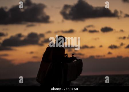 12. Oktober 2022, Gaza-Stadt, der Gazastreifen, Palästina: Palästinenser sitzen während des Sonnenuntergangs westlich des zentralen Gazastreifens am Ufer des Mittelmeers. (Bild: © Mahmoud Issa/Quds Net News via ZUMA Press Wire) Stockfoto