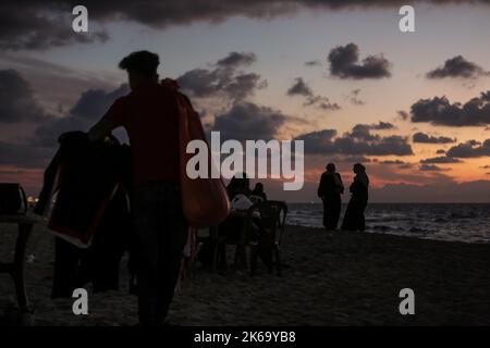 12. Oktober 2022, Gaza-Stadt, der Gazastreifen, Palästina: Palästinenser sitzen während des Sonnenuntergangs westlich des zentralen Gazastreifens am Ufer des Mittelmeers. (Bild: © Mahmoud Issa/Quds Net News via ZUMA Press Wire) Stockfoto