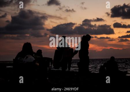 12. Oktober 2022, Gaza-Stadt, der Gazastreifen, Palästina: Palästinenser sitzen während des Sonnenuntergangs westlich des zentralen Gazastreifens am Ufer des Mittelmeers. (Bild: © Mahmoud Issa/Quds Net News via ZUMA Press Wire) Stockfoto