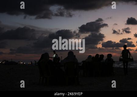 12. Oktober 2022, Gaza-Stadt, der Gazastreifen, Palästina: Palästinenser sitzen während des Sonnenuntergangs westlich des zentralen Gazastreifens am Ufer des Mittelmeers. (Bild: © Mahmoud Issa/Quds Net News via ZUMA Press Wire) Stockfoto