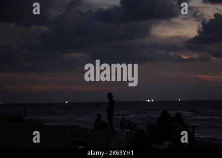12. Oktober 2022, Gaza-Stadt, der Gazastreifen, Palästina: Palästinenser sitzen während des Sonnenuntergangs westlich des zentralen Gazastreifens am Ufer des Mittelmeers. (Bild: © Mahmoud Issa/Quds Net News via ZUMA Press Wire) Stockfoto