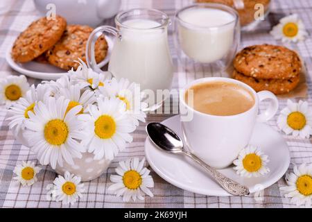 Ländliches Frühstückskonzept. Kaffee, Milch und Kekse auf dem Tisch mit schönen Gänseblümchen. Stockfoto