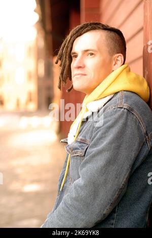 Porträt eines jungen, positiven Mannes mit Dreadlocks, die an einer Wand auf der Straße der Stadt stehen Stockfoto