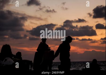 12. Oktober 2022, Gaza-Stadt, der Gazastreifen, Palästina: Palästinenser sitzen während des Sonnenuntergangs westlich des zentralen Gazastreifens am Ufer des Mittelmeers. (Bild: © Mahmoud Issa/Quds Net News via ZUMA Press Wire) Stockfoto