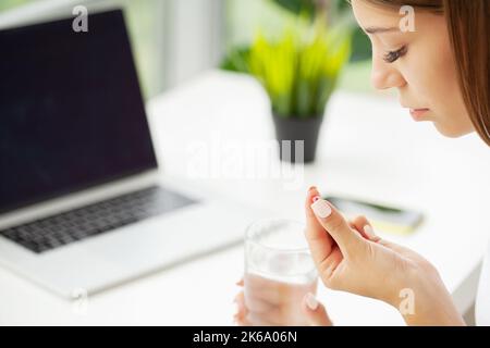 Frau, die eine Pille mit Cod Liver Oil Omega-3 eingenommen hat und morgens Ein Glas frisches Wasser hält Stockfoto