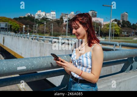 Eine junge Rotschopf-Frau, die Nachrichten auf ihrem Handy überprüft und lächelt. Speicherplatz kopieren. Ausrichtung im Querformat. Stockfoto