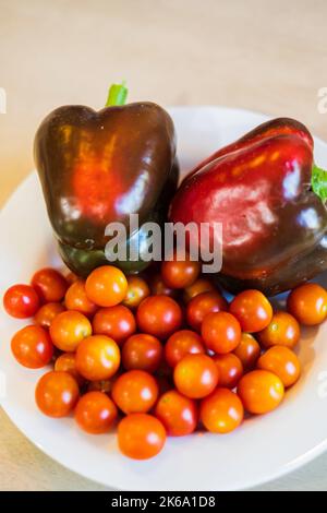 Kirschtomaten oder Traubentomaten. Selbst gewachsen. Unbestimmte, hybride Sorte. Super Sweet 100 Sorte, mit roten Paprika, Capsicum annuum. Stockfoto
