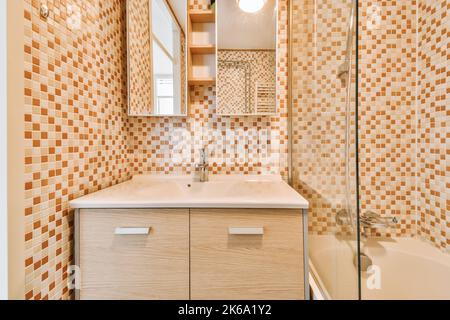 Badewanne mit Glasdusche in der Ecke neben Waschbecken und Spiegel im kleinen hellen Badezimmer mit weißen Kachelwänden Stockfoto