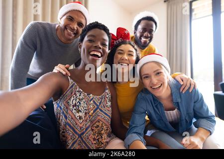 Bild von fröhlichen, vielfältigen Freunden, die zu Hause weihnachten feiern und Selfie machen Stockfoto