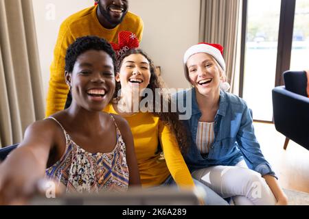 Bild von fröhlichen, vielfältigen Freunden, die zu Hause weihnachten feiern und Selfie machen Stockfoto